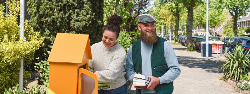 man en vrouw zetten boeken in minibieb op straat