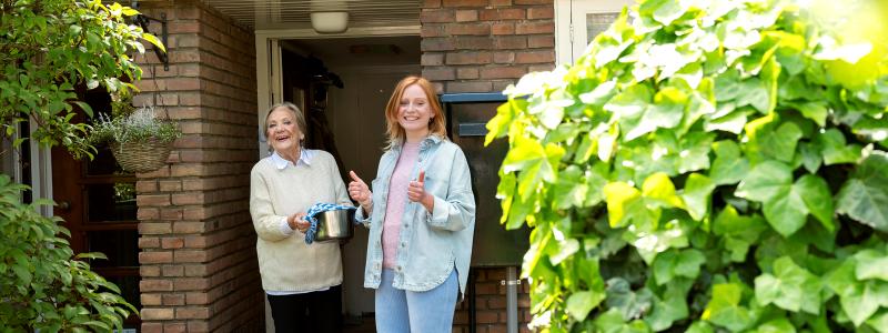 jonge vrouw geeft oma pan met eten bij voordeur